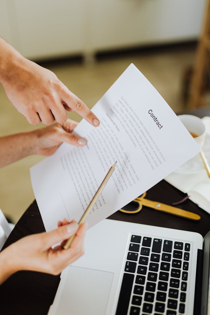services-01 Hands pointing at contract on desk with laptop, indicating collaboration