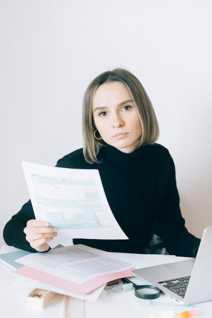 services-03 Caucasian woman in black sweater reviewing documents at a desk with paperwork and a laptop.